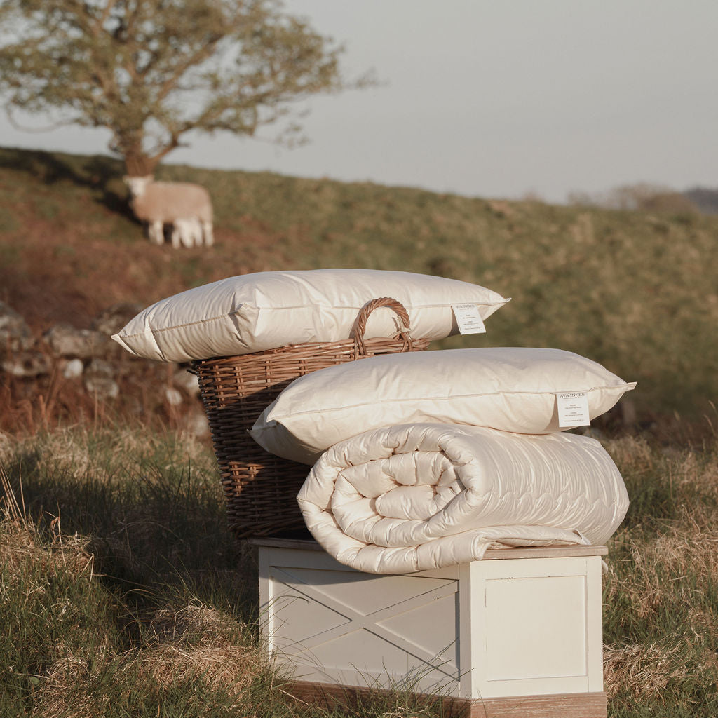 Stack of pillows and a quilt on a wooden box with a pastoral background