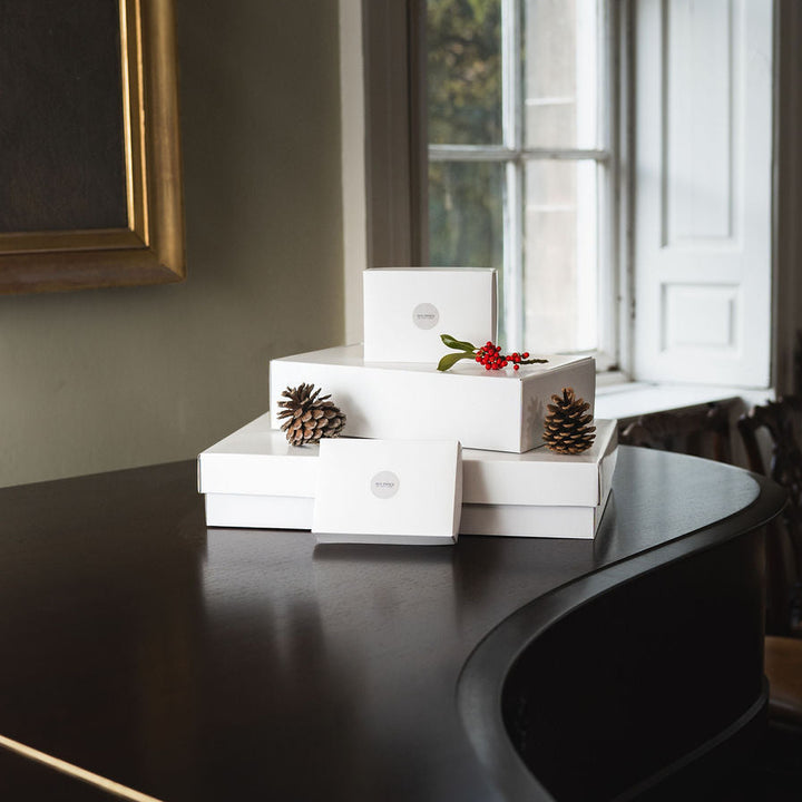 White decorative boxes on a dark piano with a window in the background